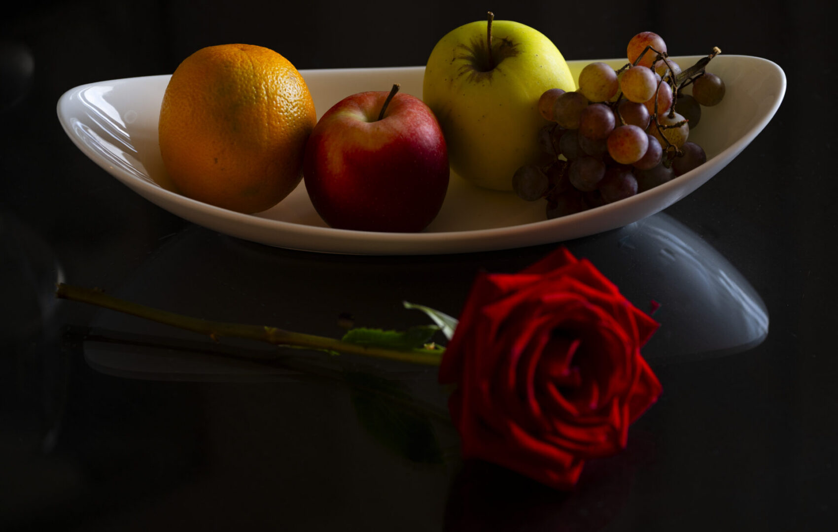 Fruit bowl with rose on black surface